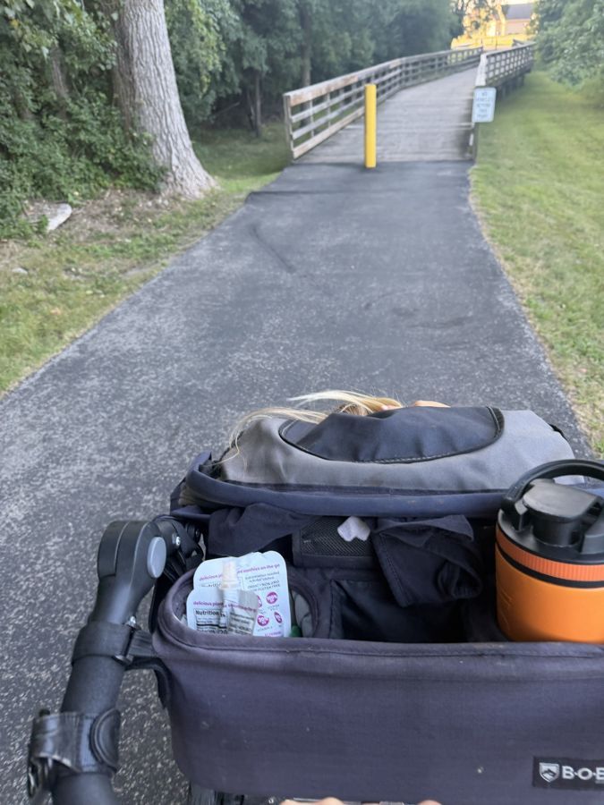 View from the handlebar of a jogging stroller heading toward a wooden footbridge on a paved trail.